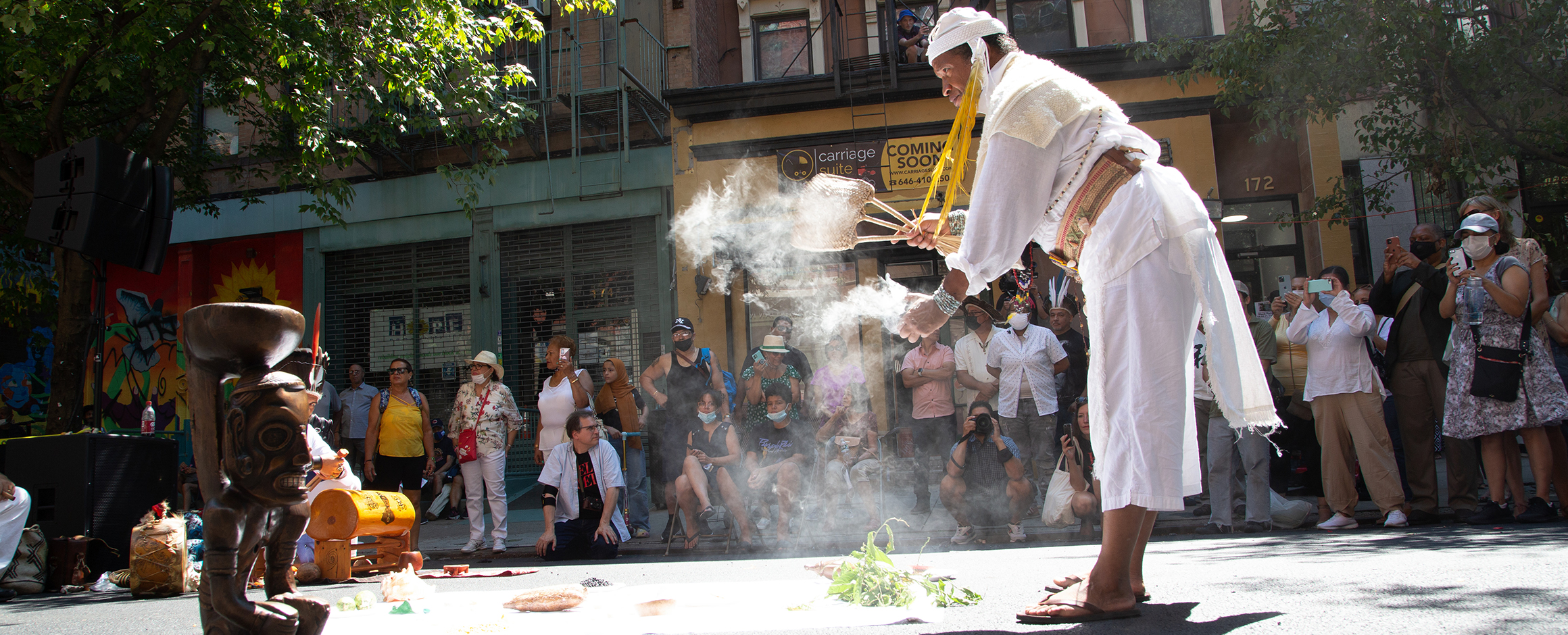 A crowd watches as a member of the Caney Indigenious Spiritual Circle performs a ritual with a replica of a Cemí Cohobabat stand at Miguel Luciano’s culminating community event in El Barrio.