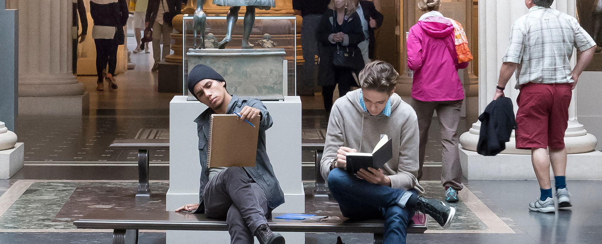 Two young men sit on a bench drawing in the Greek and Roman gallery