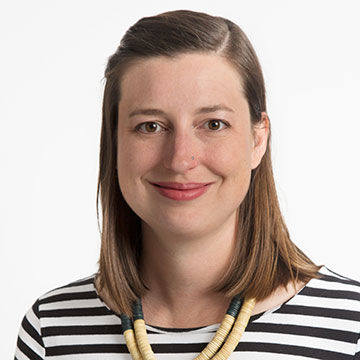 A smiling woman with medium length straight brown hair, wearing a black and white striped top and bead necklace