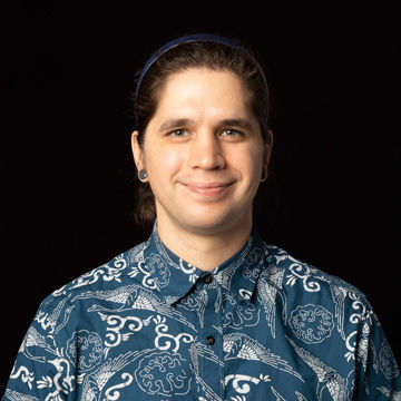 A smiling man with hair pulled back in a blue headband, wearing a blue patterned button-down shirt