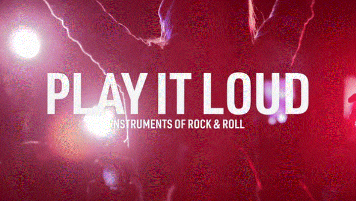 A woman raises her hands, silhouetted against red stage lights at a rock concert