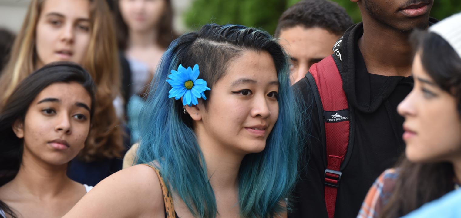 A group of teenagers and a teenage girl with blue hair in the middle wait outside the museum before a Teens Take the Met event