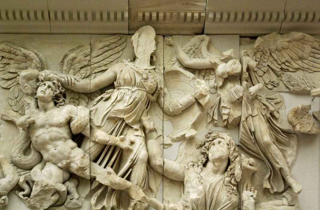 A stone carving of 4 figures, two of which have wings. Some of the work is damaged, and they are missing chunks or features